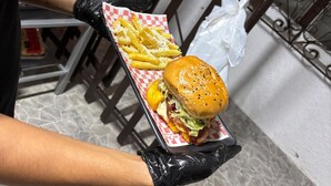 Una persona sosteniendo una bandeja con una hamburguesa y papas fritas.