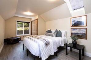 Une chambre avec un grand lit, une fenĂȘtre, un puits de lumiĂšre et deux tableaux encadrĂ©s accrochĂ©s au mur.