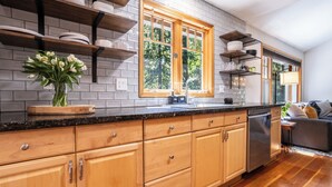 Una cocina con armarios de madera, encimera negra, ventana con vista a árboles y lavavajillas.