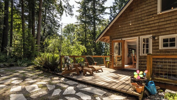 Una cabaña de madera con terraza, sendero de piedra y mobiliario exterior.