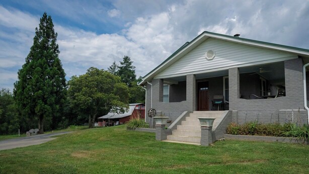 A single-story house with a front porch, a small front yard, and a large tree to the left.
