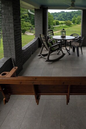 Un patio techado con una mesa, sillas y una hamaca, con vistas a un paisaje verde.