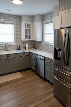 Una cocina con armarios grises, un refrigerador de acero inoxidable y suelo de madera.