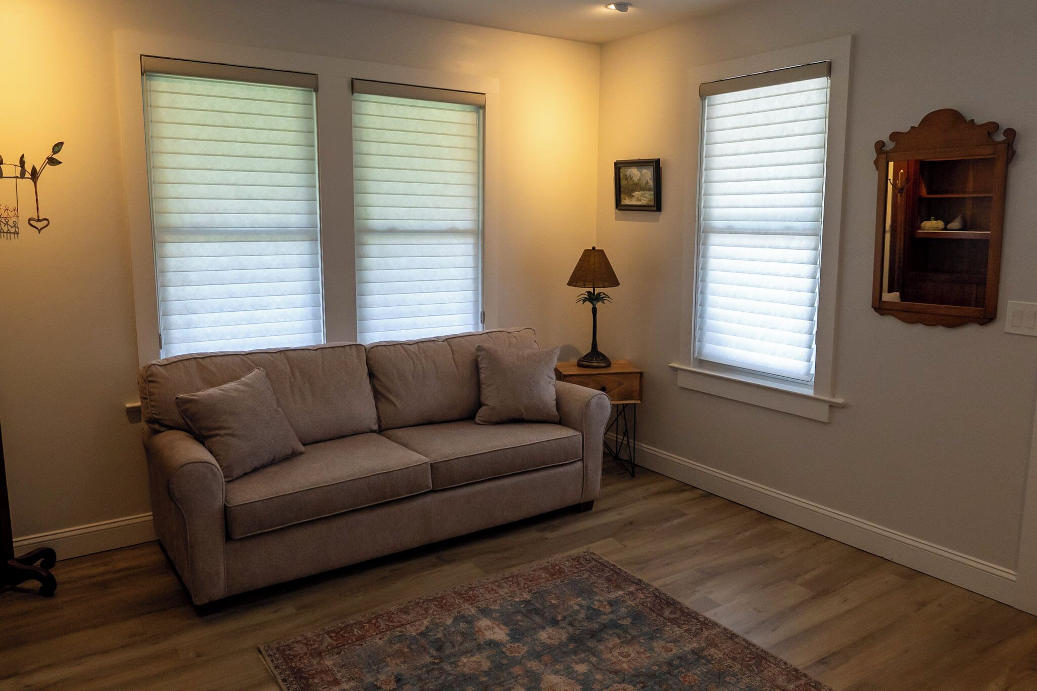 A living room with a beige sofa, a patterned rug, and two windows with blinds.