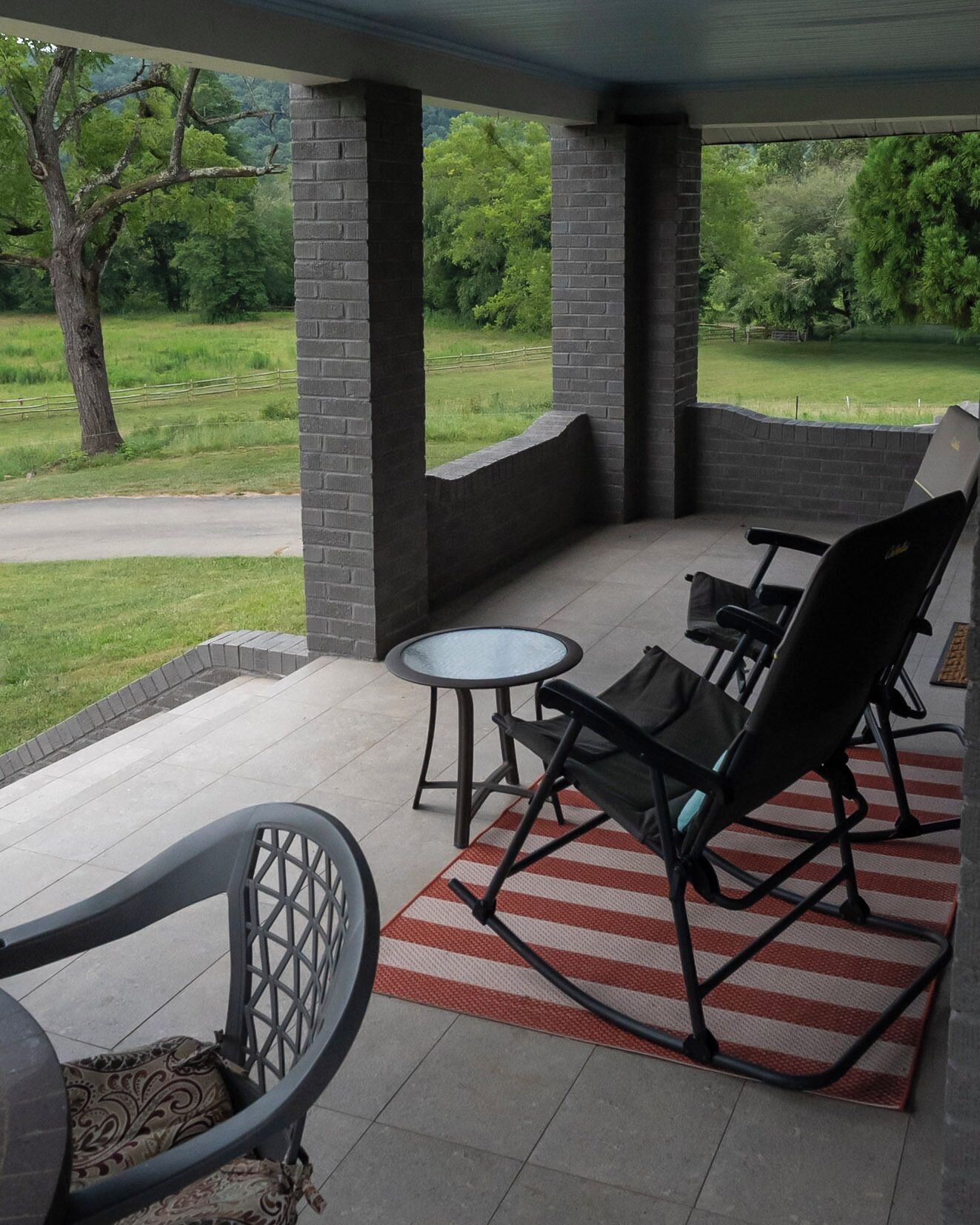 A covered patio area with brick pillars, a table, two chairs, and a red and white striped rug.