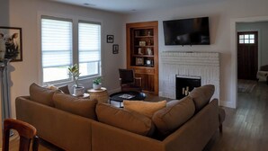 A living room with a sectional sofa, a fireplace, a bookshelf, and a TV mounted on the wall.