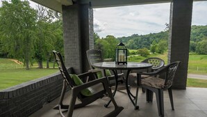 A covered patio with a round table and chairs, a lantern, and a view of a green landscape.