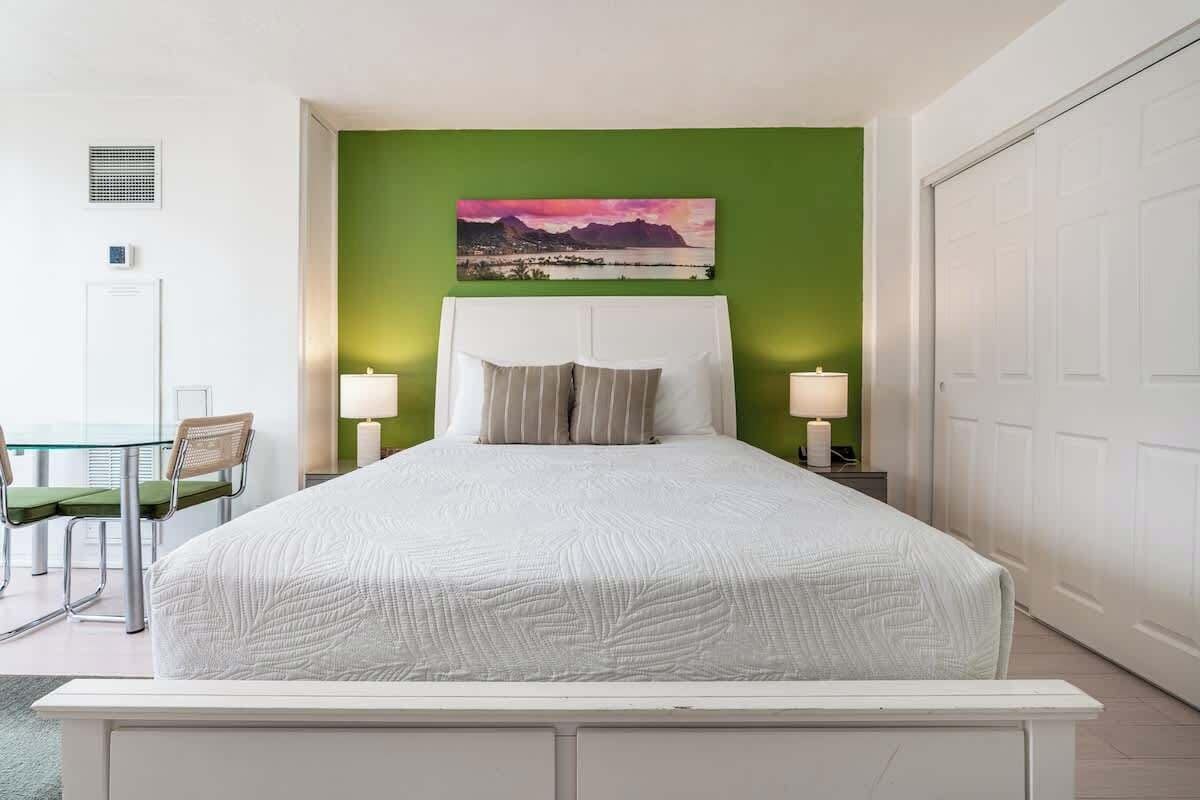 Hotelkamer met groot bed, groene accentmuur, schilderij, bureau met stoel en een witte deur.