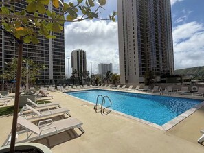 Ein Pool auf dem Dach mit Liegestühlen, umgeben von Hochhäusern.