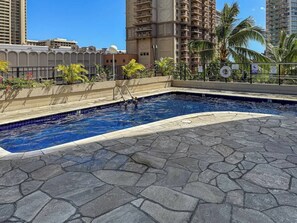 A swimming pool with a stone deck, surrounded by palm trees and a cityscape in the background. - Renovated Studio, Steps to Waikiki Beach, Parking (Honolulu)