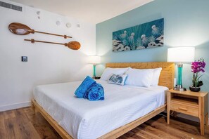 A neatly made bed with white bedding, a wooden headboard, and a painting of marine life above it. - Renovated Studio, Steps to Waikiki Beach, Parking (Honolulu)