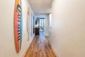 A hallway with wooden flooring, a surfboard decoration, and a view to a balcony. - Ocean View Studio, Newly Renovated, Free Parking (Honolulu)