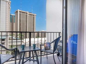 A balcony with a table, chairs, and a view of high-rise buildings. - Ocean View Studio, Newly Renovated, Free Parking (Honolulu)