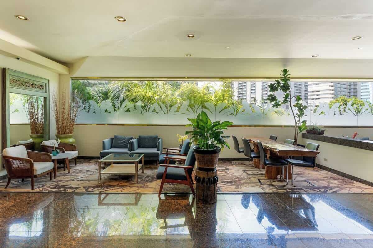 A spacious lobby with a large dining table, comfortable seating, and a view of greenery through frosted glass windows.