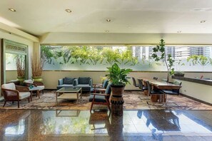 A spacious lobby with a large dining table, comfortable seating, and a view of greenery through frosted glass windows. - Central Waikiki Studio, City View, Pool, 2 Queens (Honolulu)