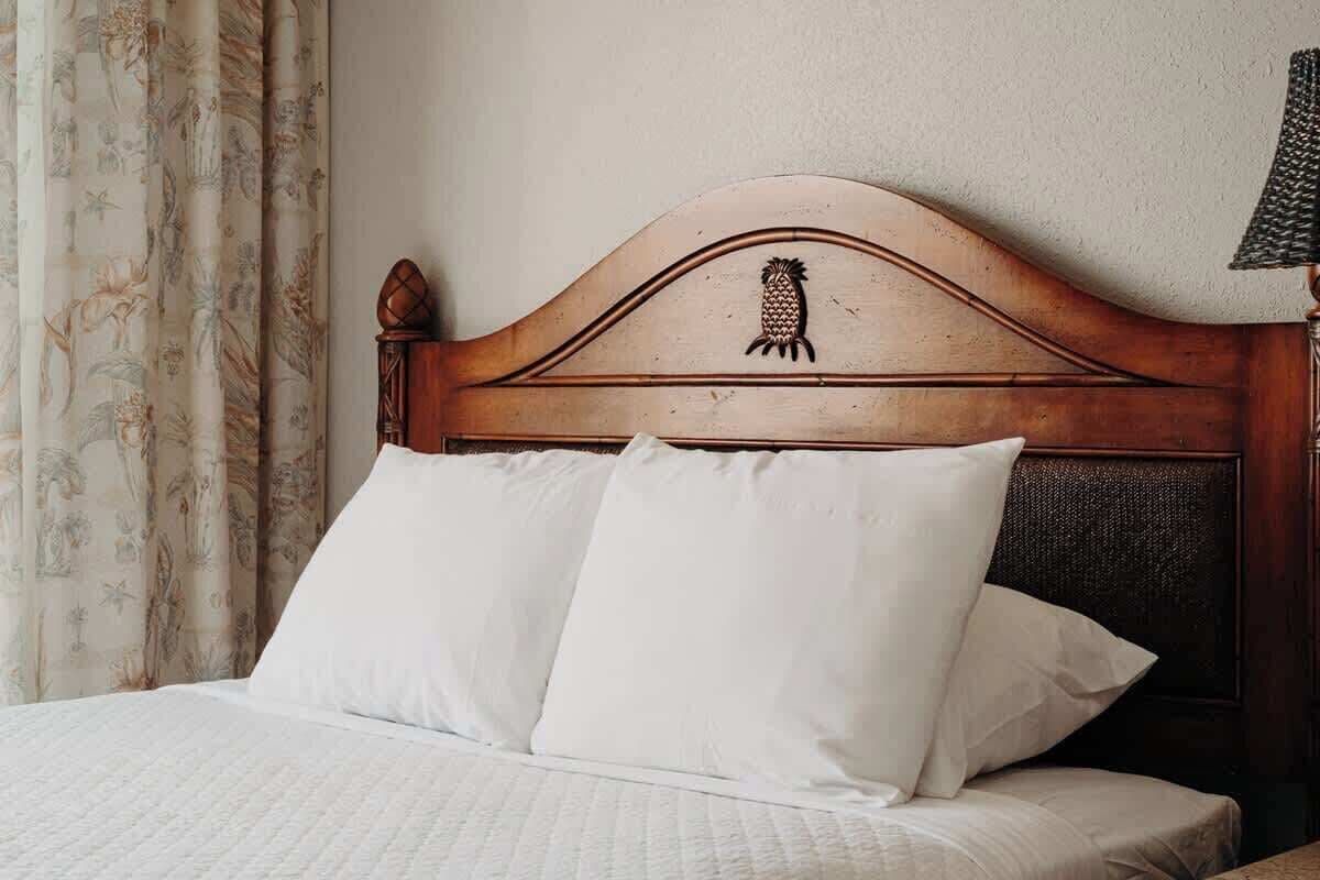 Una cama con cabecera de madera, ropa de cama blanca y cortina con estampado floral.