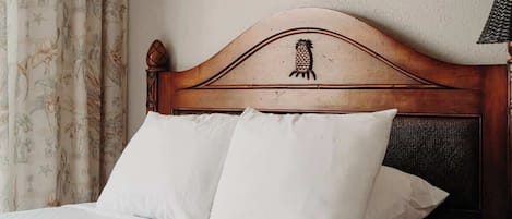 Una cama con cabecera de madera, ropa de cama blanca y cortina con estampado floral.
