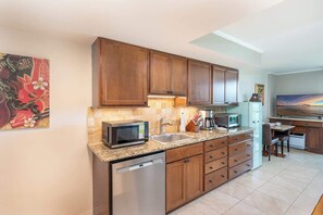 A kitchen with wooden cabinets, a microwave, a coffee maker, and a dishwasher. - Central Waikiki Studio, City View, Pool, 2 Queens (Honolulu)