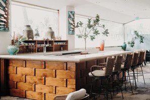 A bar area with a wooden counter, wicker chairs, and a large window with a view. - Central Waikiki Studio, City View, Pool, 2 Queens (Honolulu)