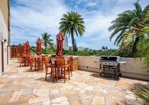 An outdoor patio with stone flooring, wooden chairs, and a grill. - Central Waikiki Studio, City View, Pool, 2 Queens (Honolulu)