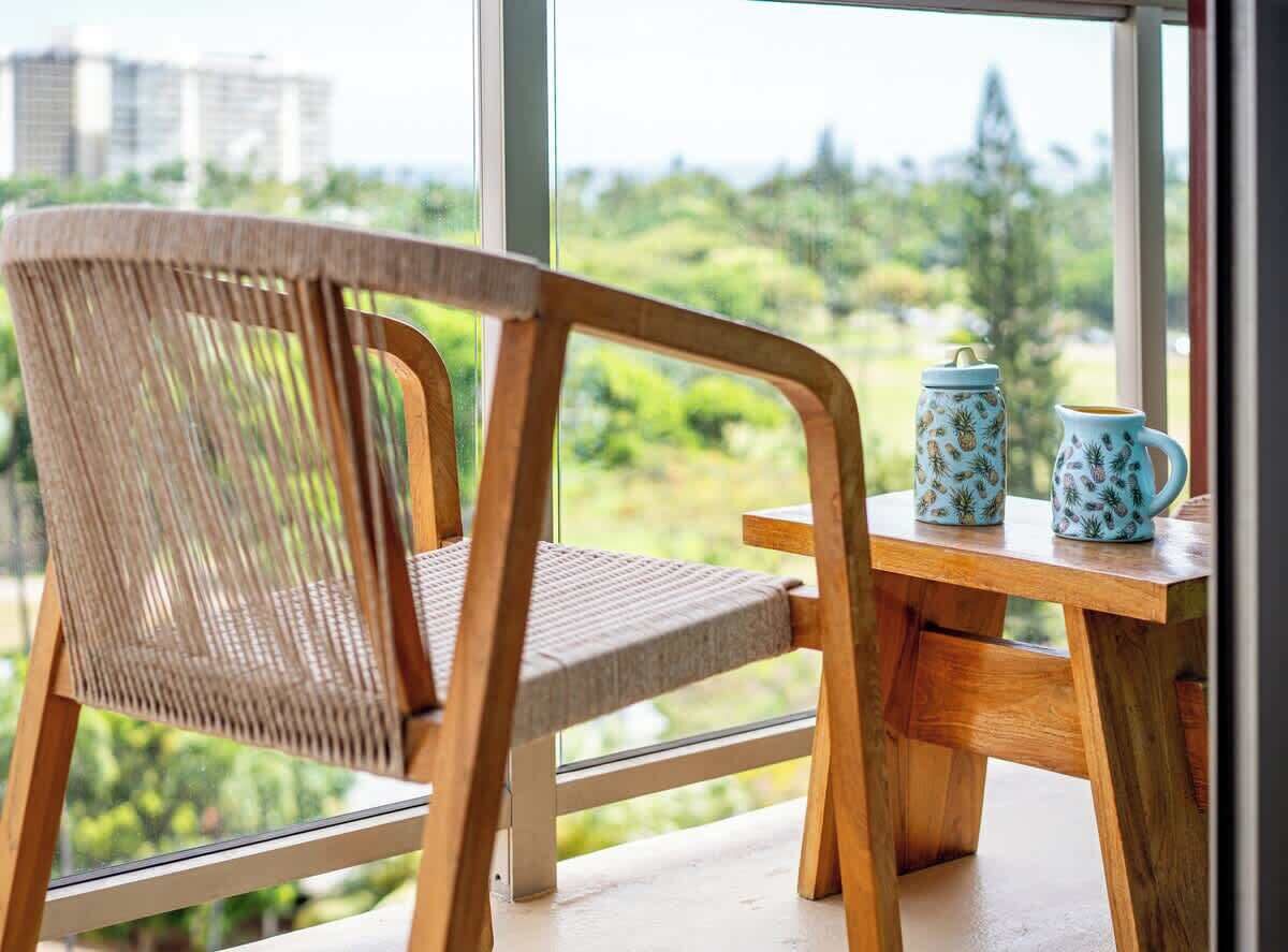 A wooden chair and table by a window with a view of greenery and buildings.