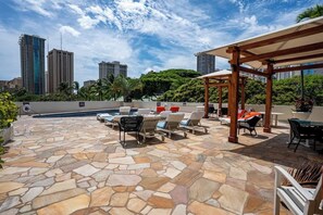A rooftop patio with stone flooring, lounge chairs, a pool, and a city skyline in the background. - Central Waikiki Studio, City View, Pool, 2 Queens (Honolulu)