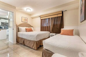 A hotel room with two beds, a radiator, a painting on the wall, and a view of the kitchen through an open door. - Central Waikiki 2 Bedroom, AC, Lanai, Pool, King (Honolulu)