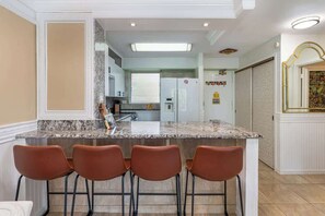 Une cuisine dotée d’un plan de travail en marbre, de quatre tabourets de bar, d’un réfrigérateur et d’une fenêtre.