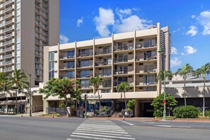 A multi-story hotel with balconies, a clear sky, and palm trees. - Heart of Waikiki | Walkable, King Bed, Beach Gear. (Honolulu)
