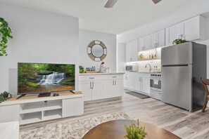 A modern kitchen with white cabinets, a stainless steel refrigerator, and a flat-screen TV on a white entertainment unit. - Heart of Waikiki | Walkable, King Bed, Beach Gear. (Honolulu)