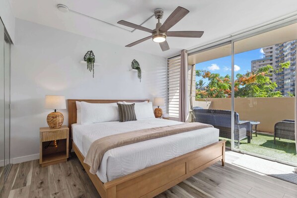 A bedroom with a bed, bedside tables, a ceiling fan, and a balcony with outdoor furniture. - Heart of Waikiki | Walkable, King Bed, Beach Gear. (Honolulu)