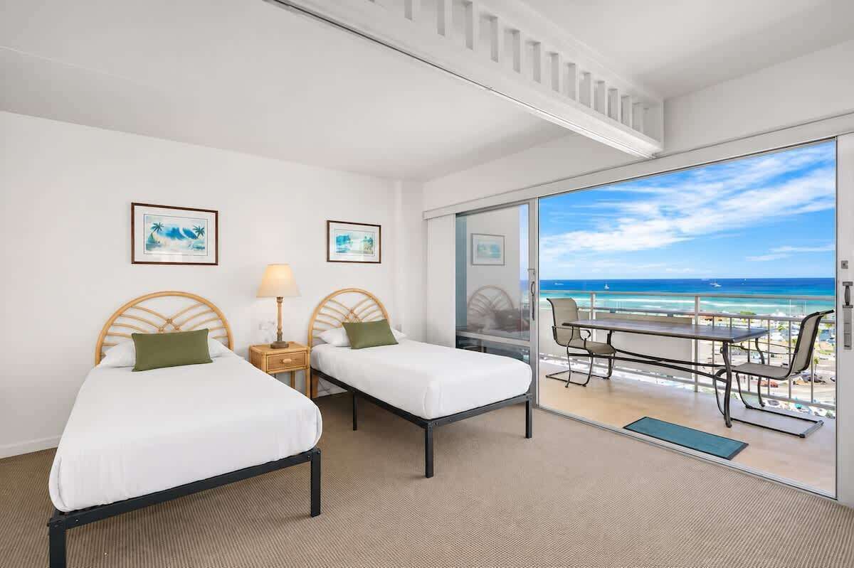 A hotel room with two beds, a balcony with a table and chairs, and a view of the ocean.