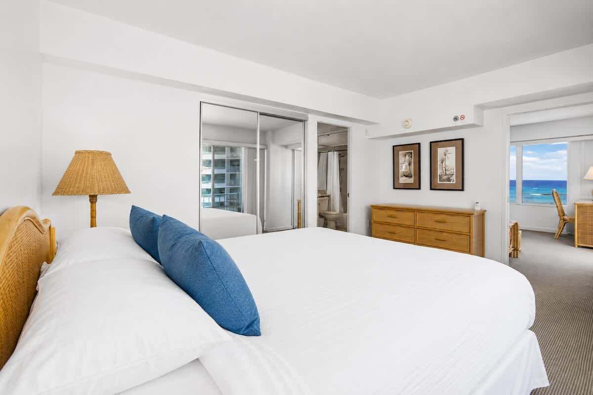 A hotel room with a bed, a wardrobe, a desk, and a view of the ocean.