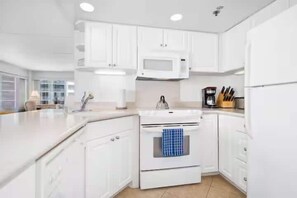 A modern kitchen with white cabinetry, a microwave, an oven, and a coffee maker. - Oceanview Marina Front, Steps to Waikiki Beach (Honolulu)