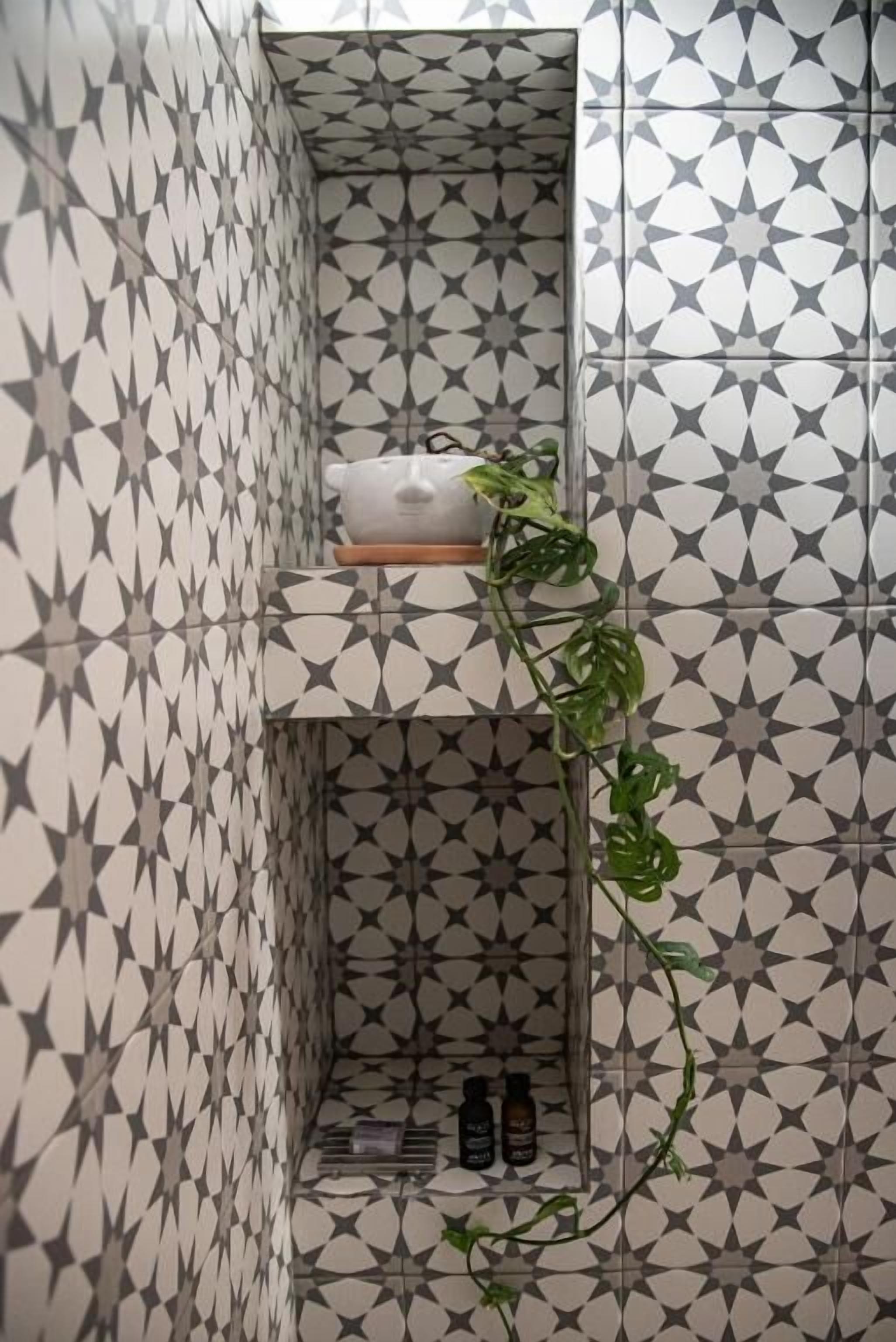 Un baño con un estampado geométrico de azulejos, una planta y un estante con artículos de aseo.