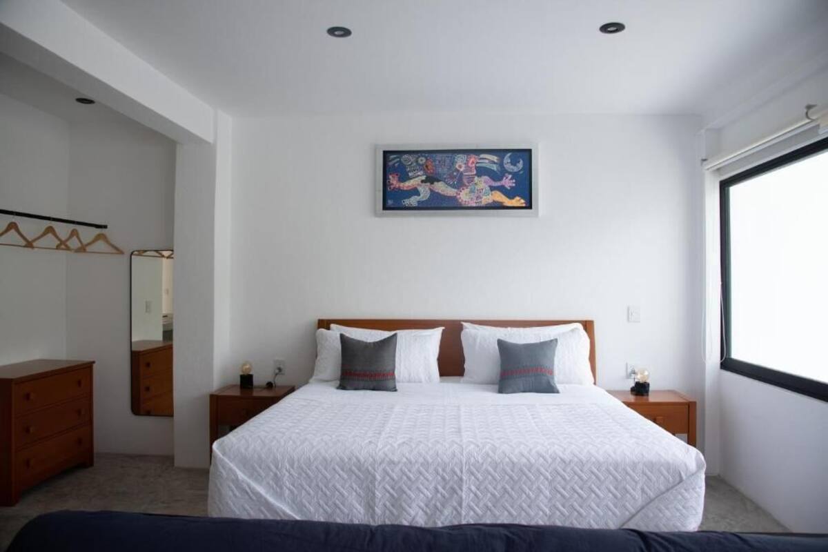 A bedroom with a bed, a nightstand, a dresser, a mirror, and a painting on the wall.