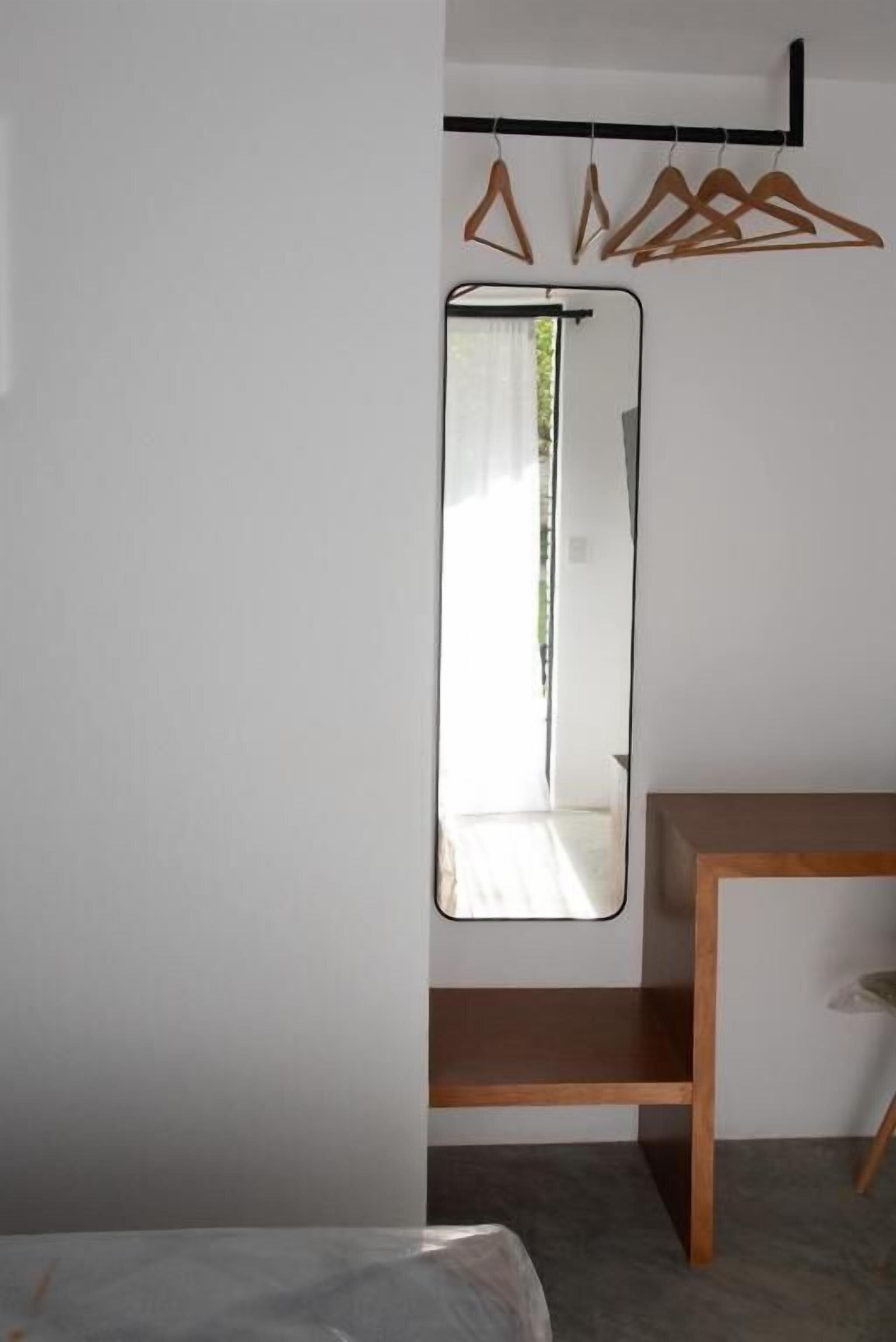Een slaapkamer met een bed, een houten nachtkastje, een spiegel en een kledingrek.