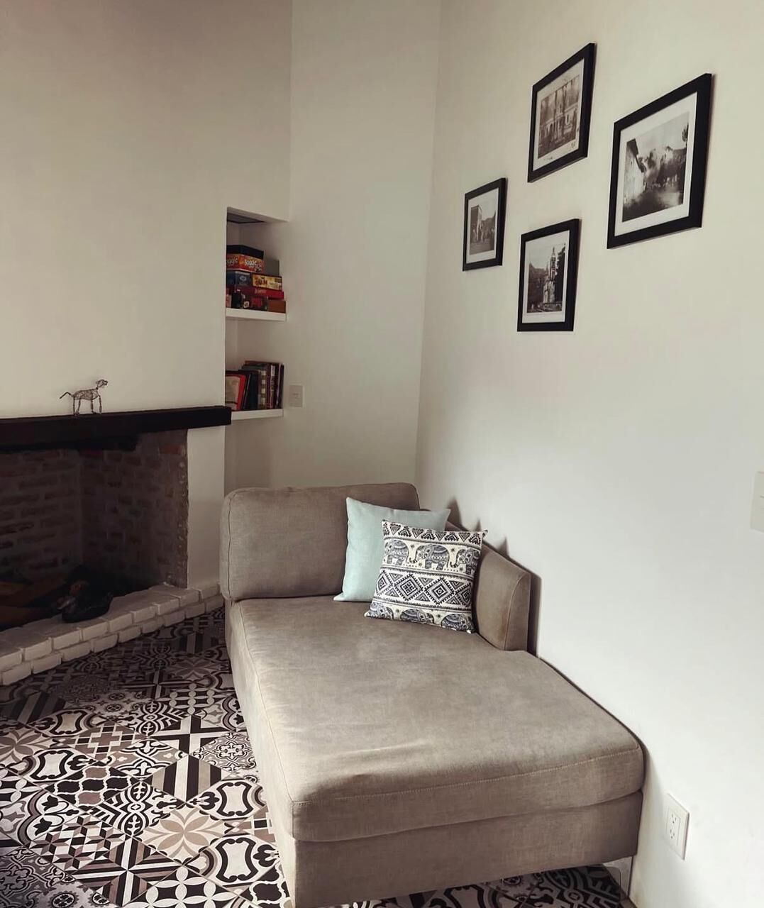 A living room with a sofa, patterned floor, fireplace, and wall-mounted pictures.
