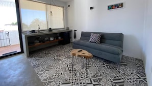 Una sala de estar moderna con un sofá gris, piso estampado, una mesita de madera y una ventana con persianas.