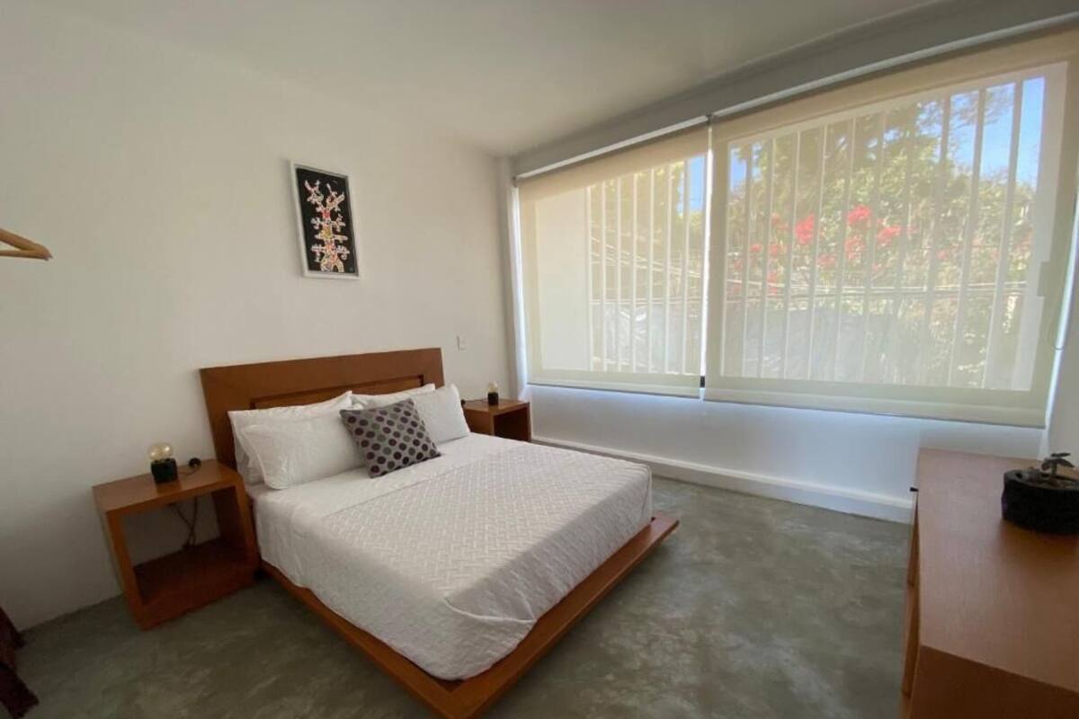 A bedroom with a bed, a nightstand, a window with blinds, and a picture on the wall.