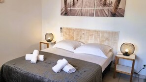 Ein ordentlich bezogenes Bett mit weißen Leinentüchern und einer grauen, strukturierten Decke, zwei Nachttischlampen und ein hölzernes Kopfteil.