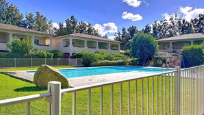 Une piscine dotée d’une terrasse en bois, entourée de pelouses bien entretenues et d’une clôture blanche.