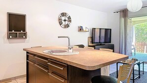 Une cuisine de taille réduite comprenant un évier, une horloge, un téléviseur et un petit coin repas.
