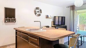Eine kleine Küche mit Spüle, einer Uhr, einem Fernseher und einer Essecke.
