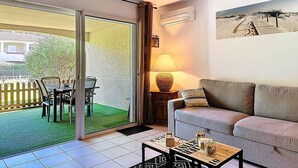 Un salon comprenant un canapé, une table basse, une lampe et une porte-fenêtre coulissante donnant sur une terrasse avec une table et des chaises.