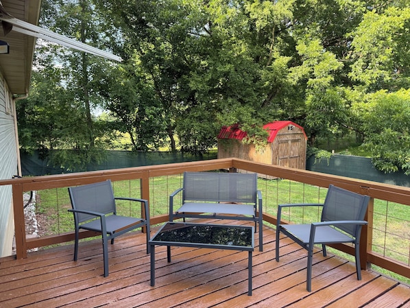 A wooden deck with three chairs and a table, surrounded by a wooden railing.