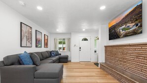 Een moderne woonkamer met een grijze hoekbank, houten vloeren, een open haard en lijstwerken aan de wanden.