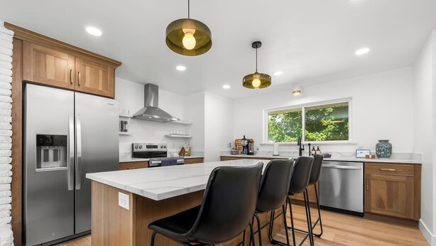 Een moderne keuken met een roestvrijstalen koelkast, een ingebouwde oven, een gasfornuis en een groot kookeiland met barstoelen.