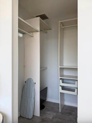 Un dressing sans porte avec des étagères ouvertes, une tringle à vêtements et une chaise à rayures.