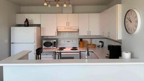 A modern kitchen with white cabinets, a microwave, stove, and a clock on the wall.